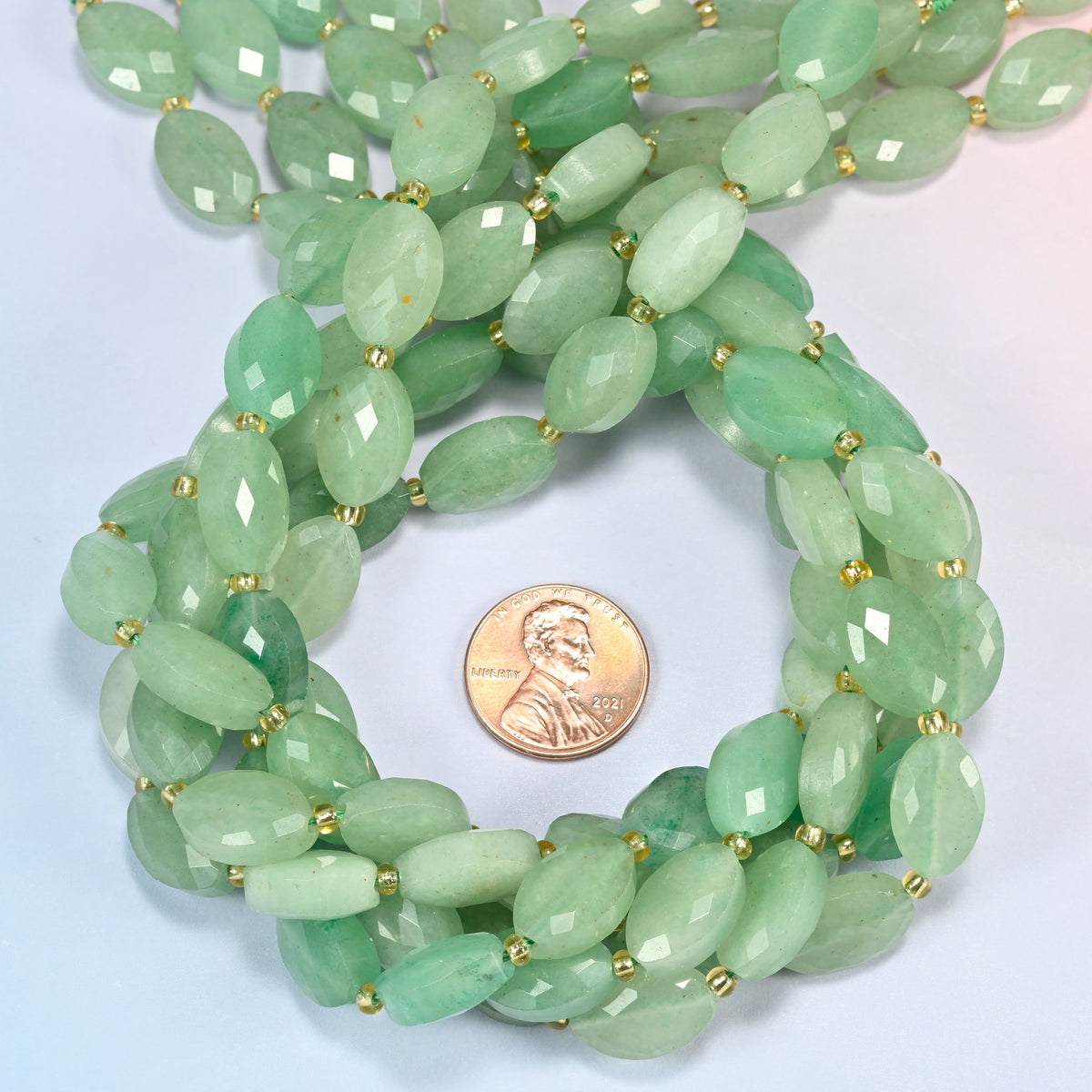 Green aventurine faceted flat oval beads 9x14mm coiled in a loop around a US penny for scale, close-up of the faceted flat oval shape