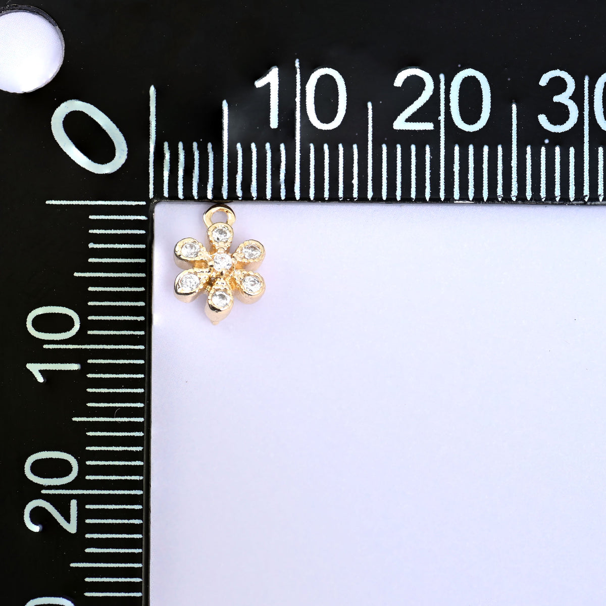 Small gold charms, one flower charm measured against a millimetre ruler