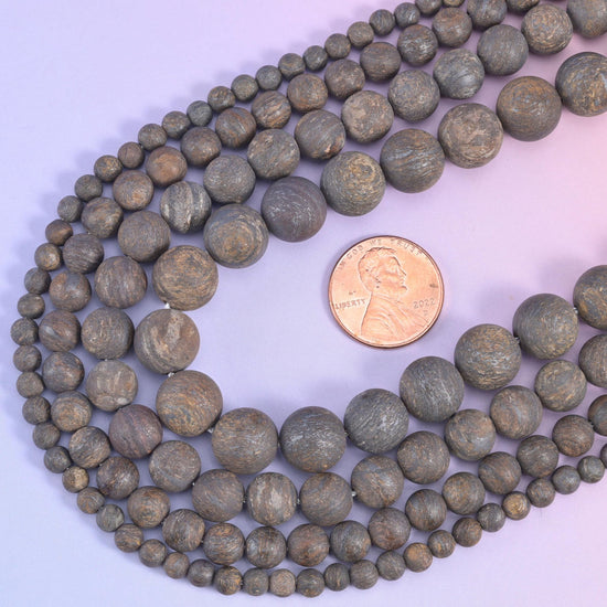 Bronzite rounds looped around a US penny so the range from small to large beads is easy to judge