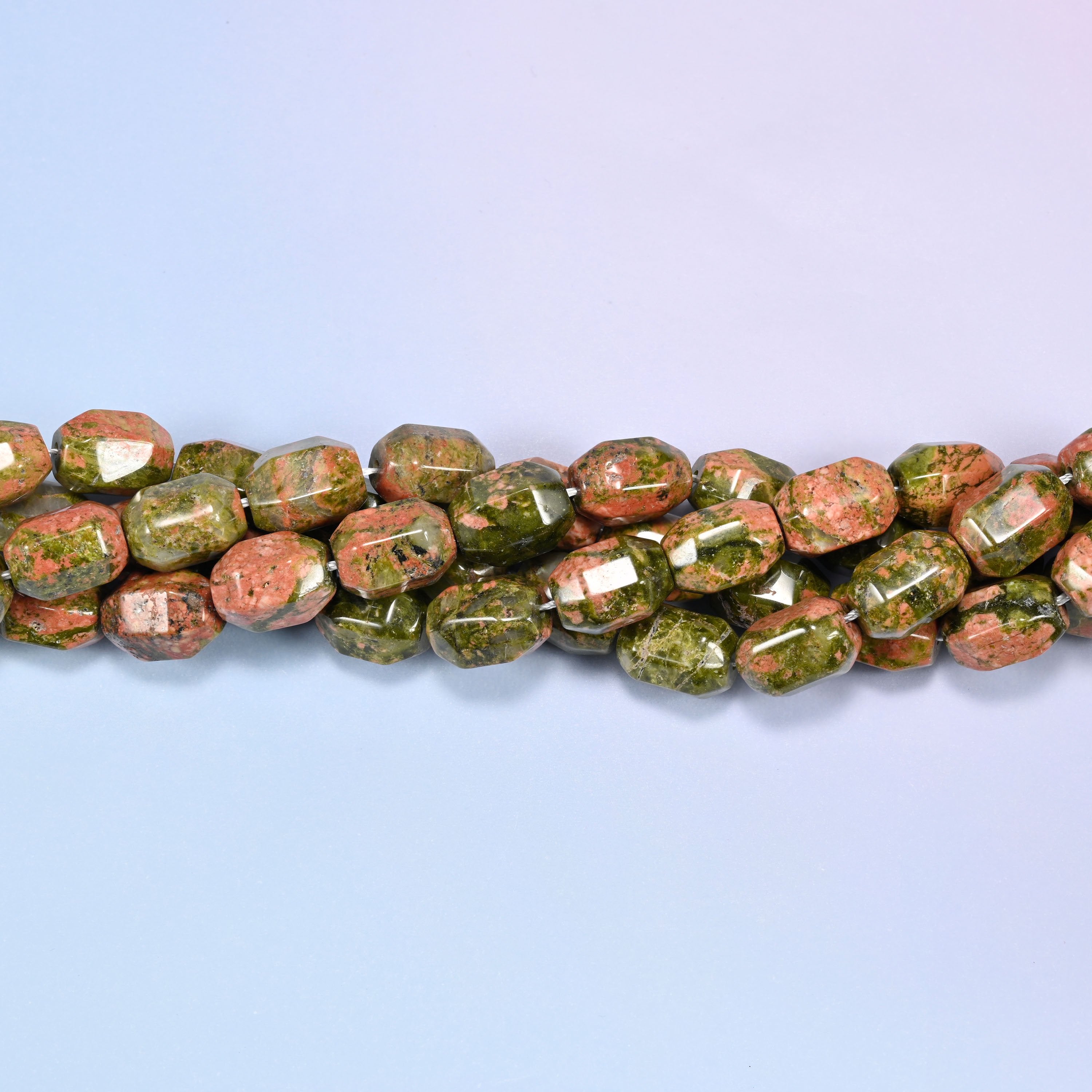 Close-up of a dense circular coil of faceted Unakite barrel beads, showing the octagonal facet cuts.