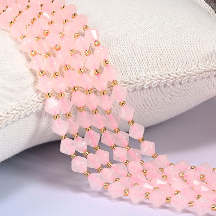 Rose Quartz faceted bicone beads draped over a cushion, close-up of the soft pink facets and gold-tone spacer beads.