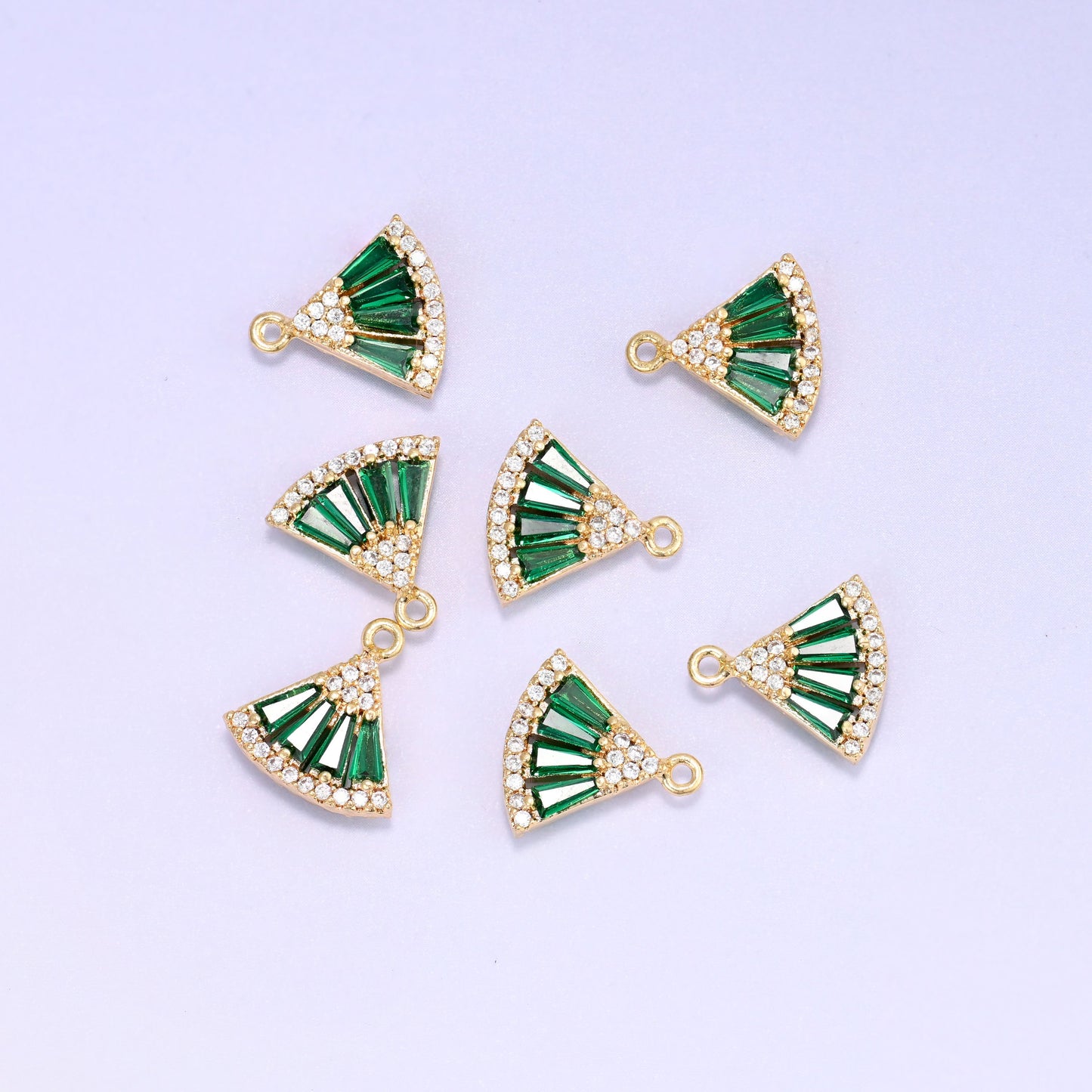 Small gold charms, seven green fan charms grouped on a pale backdrop