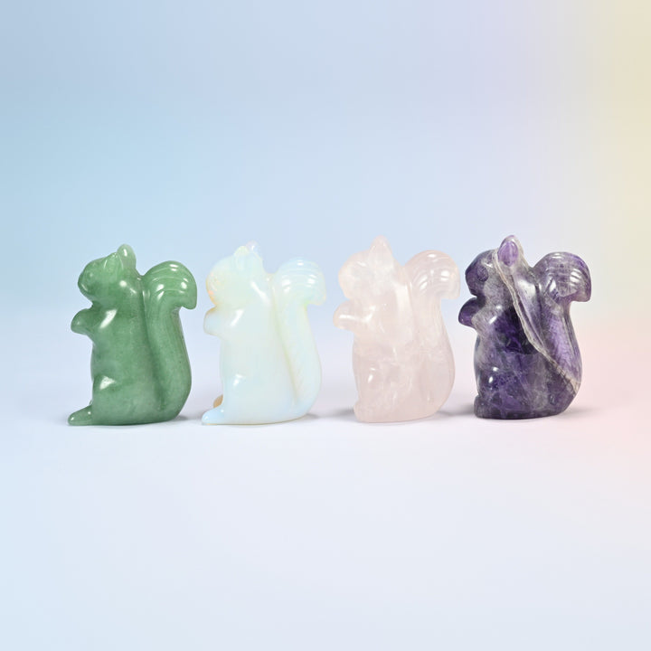 Four squirrel crystal carvings in a row: natural green aventurine, opalite, natural rose quartz and natural amethyst, side view