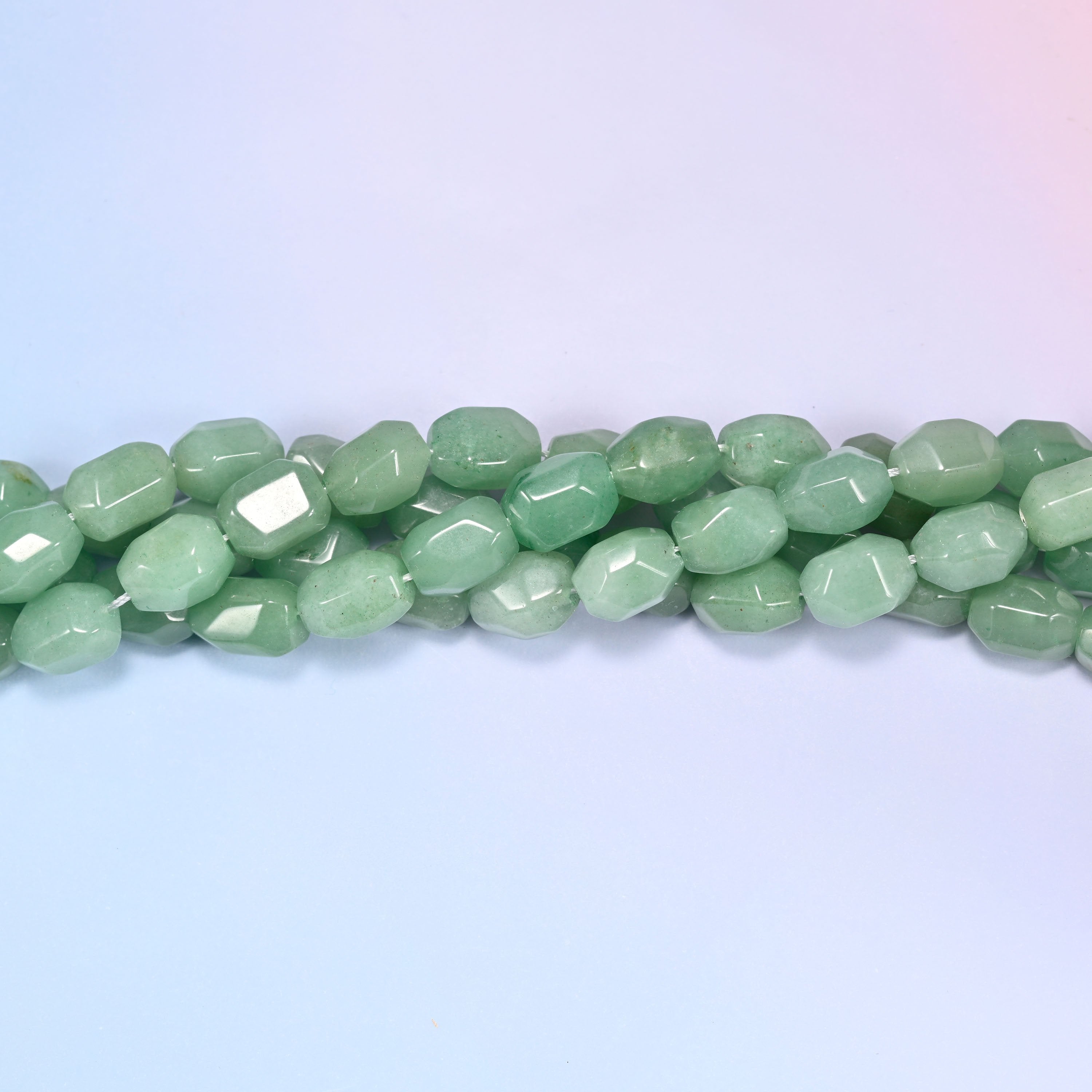 Close-up circular coil of green faceted Aventurine barrel bead strands on a lavender background with a penny in the center for size comparison.