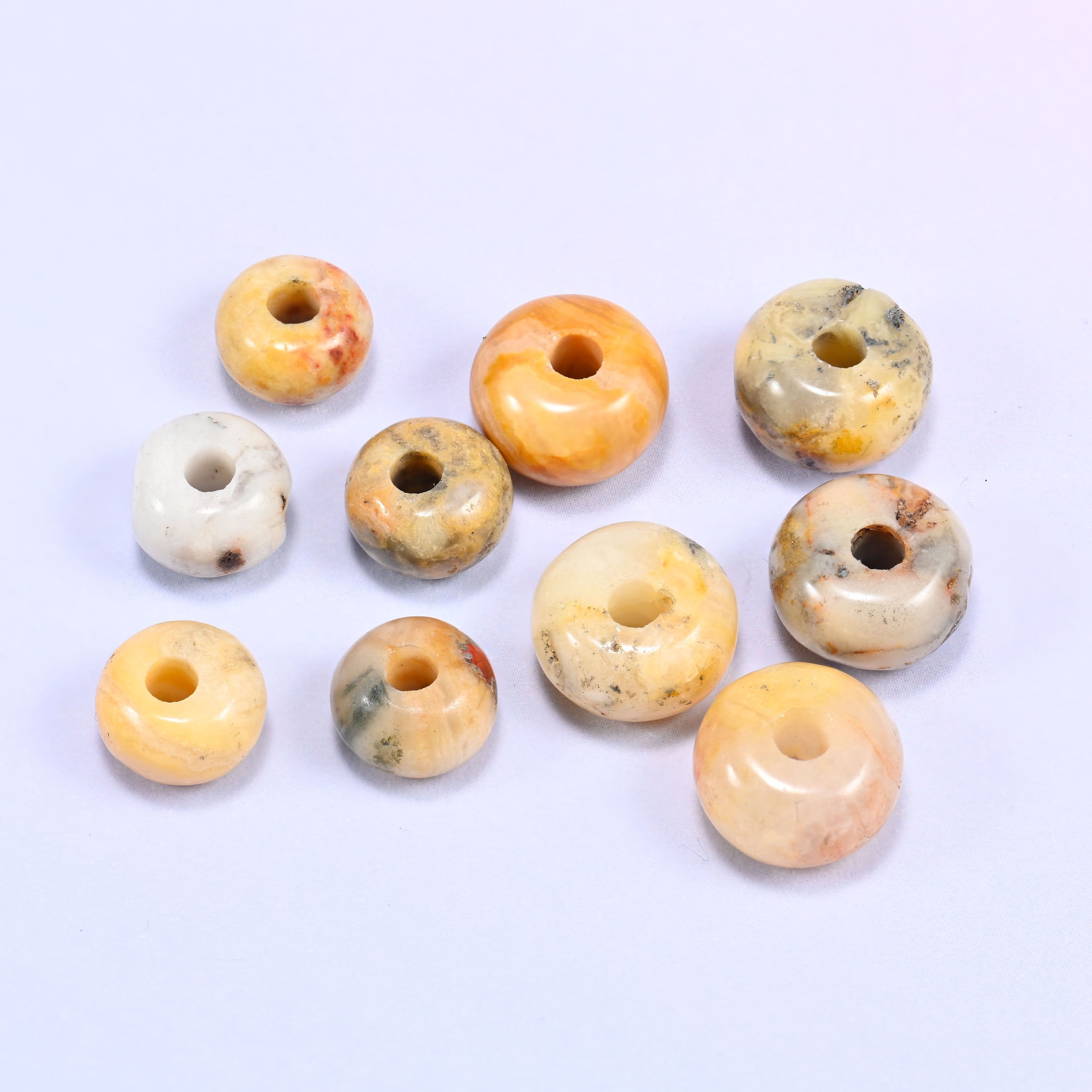 Close-up of individual loose Crazy Agate beads laid out on a white surface, showing the large center-drilled hole and varied coloring of each bead.