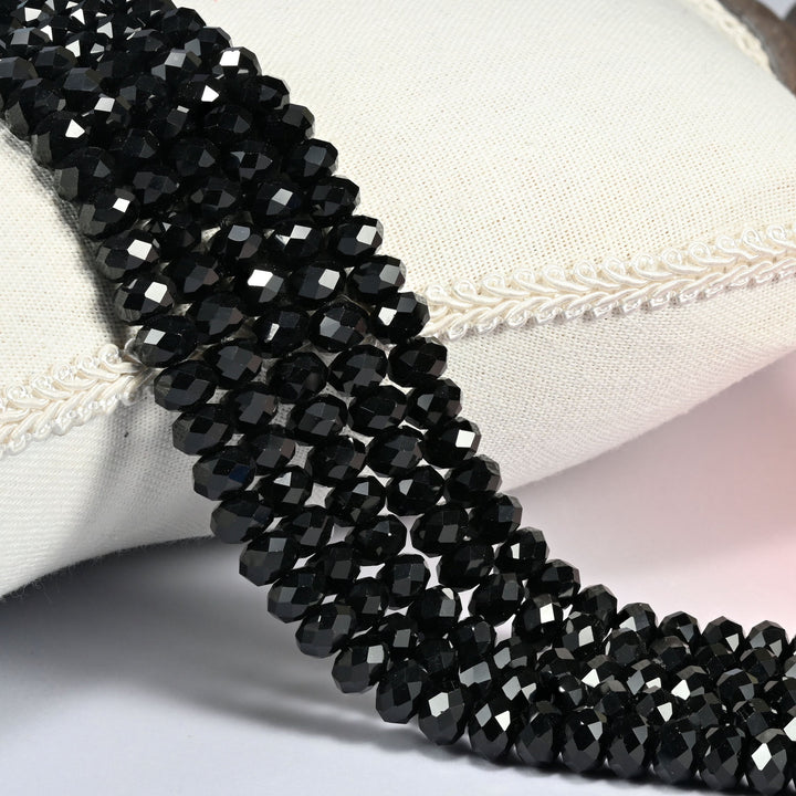 Black onyx faceted rondelle beads in jet black, several strands draped over a cream cushion with braided trim