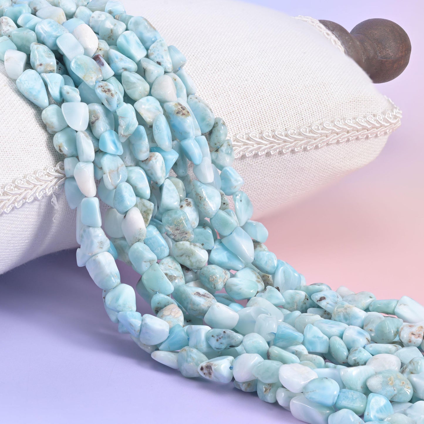 Pale blue larimar nugget strands draped over a white cushion, soft sky tones broken by white clouding