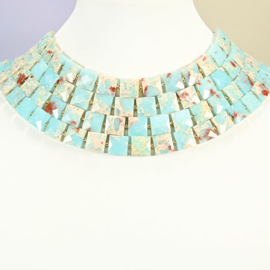 Dyed blue Shoushan stone faceted flat square strands arranged as a layered collar on a white display bust, light blue beads across the neck