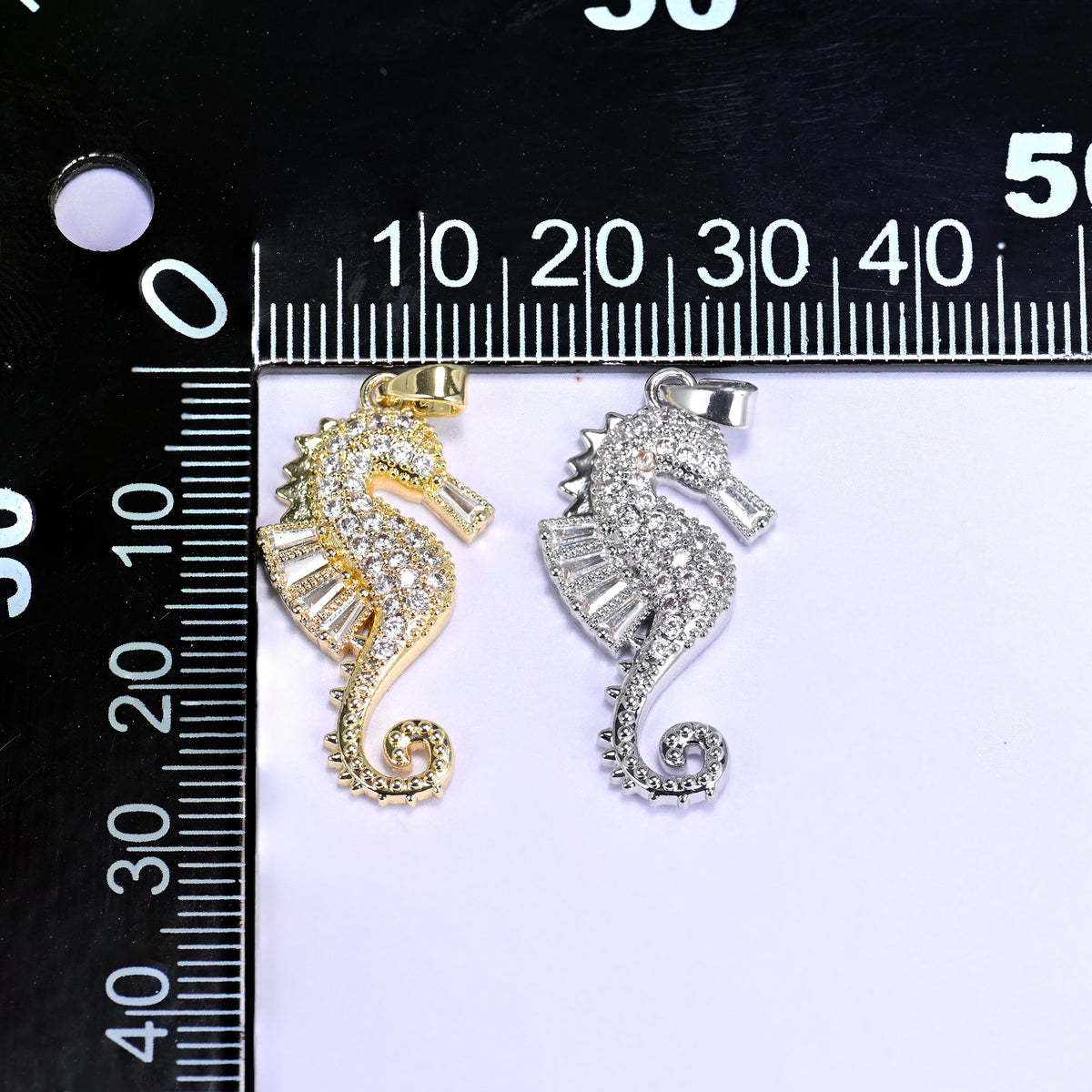 Gold and silver sea horse zirconia charms on a black millimetre ruler, shown together for size reference.