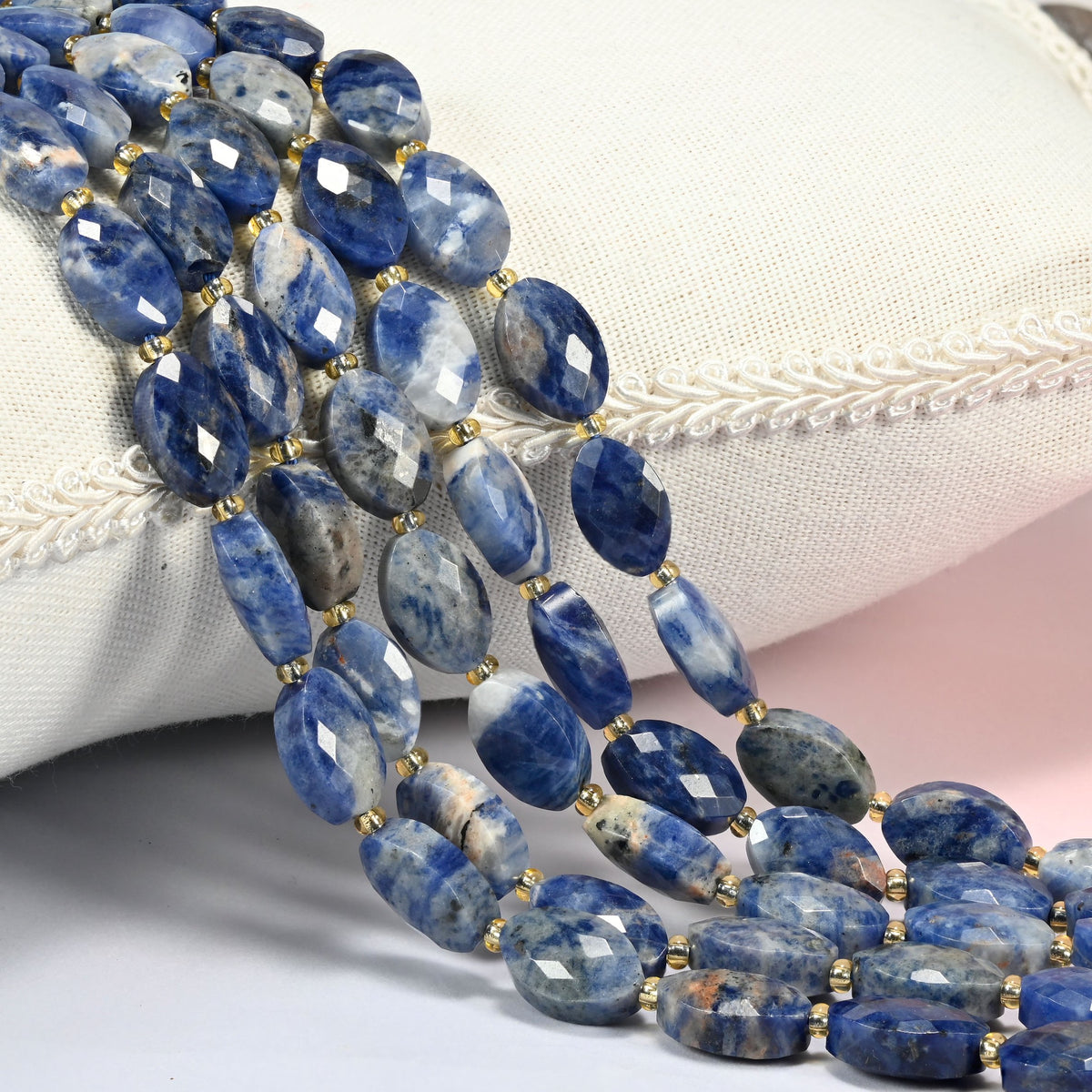 Orange sodalite faceted flat oval beads 9x14mm with small gold seed bead spacers, several strands draped over a white cushion