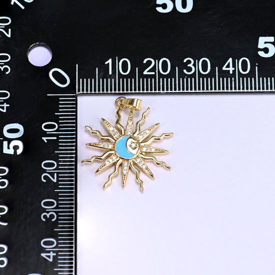 Blue enamel moon sun zirconia charm on a black millimetre ruler, the gold sunburst measuring around 26mm across.