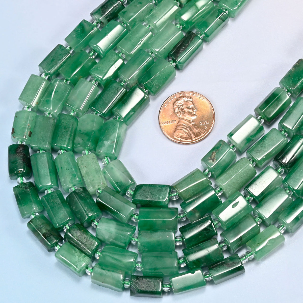 Close view of African jade faceted tube strands curving beside a US penny for scale
