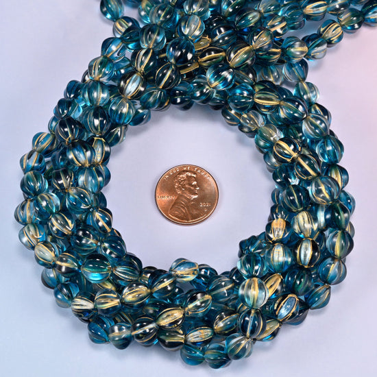 Dark blue gold pumpkin glass beads coiled tightly, shown with a US penny in the open center for scale.