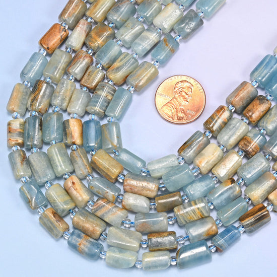 Blue calcite faceted tube beads laid in rows with a US penny resting between two strands.