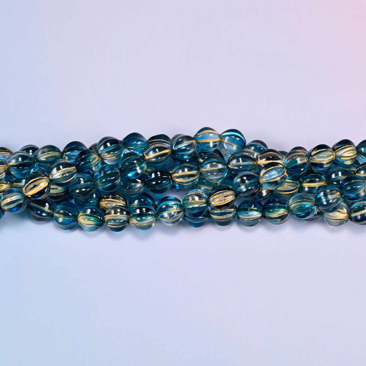 Dark blue gold pumpkin glass beads, 8mm melon rounds, strands laid in a gentle wave straight across the frame.