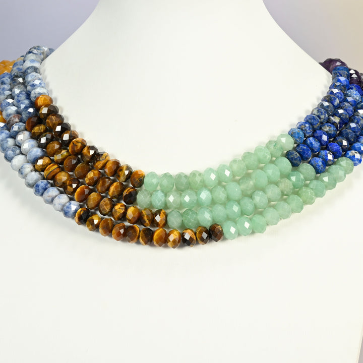 Chakra faceted rondelle strands arranged as a layered collar on a white display bust, color blocks running across the neck