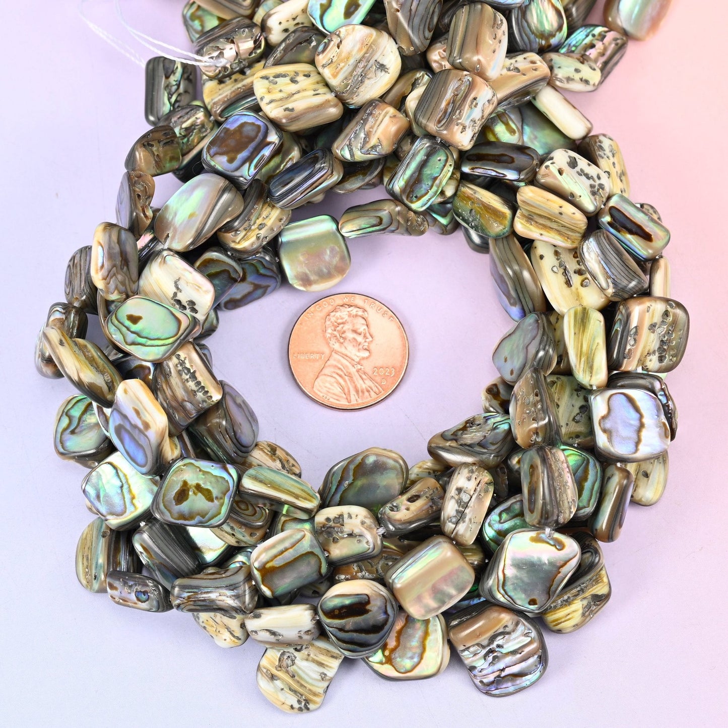 Softly squared tiles cut from natural abalone, polished on one face to reveal flashes of peacock green, teal and silvery blue over a warm smoky brown and cream ground