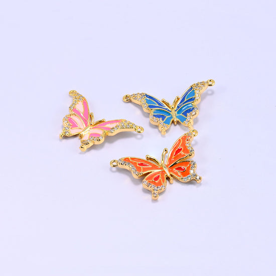 Enamel butterfly double connector pendants tilted at angles, the pink, blue and orange charms catching the light on their glossy enamel and zircon edging.