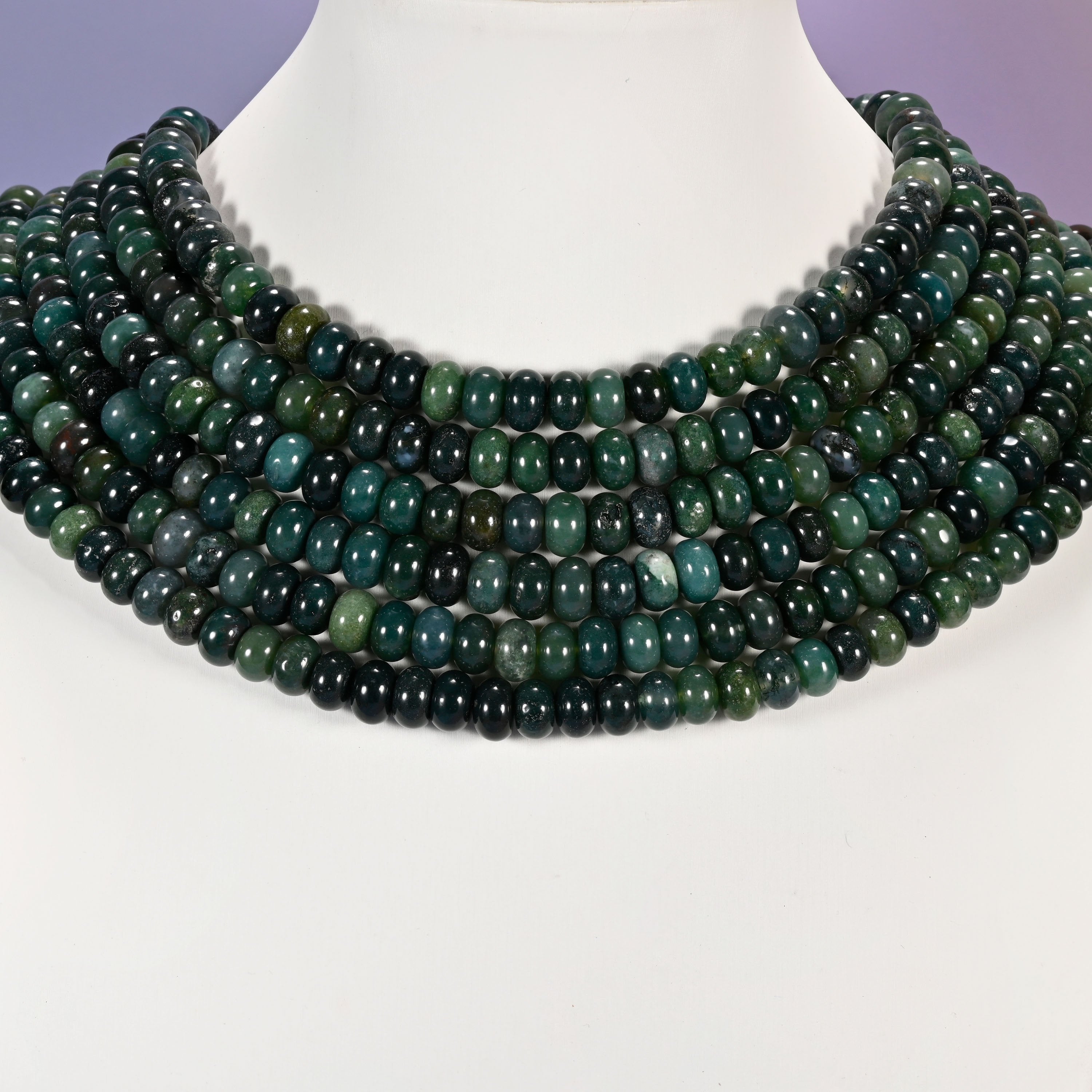 Multi-strand Moss Agate necklace laid flat on a mannequin neck form against a lavender background.