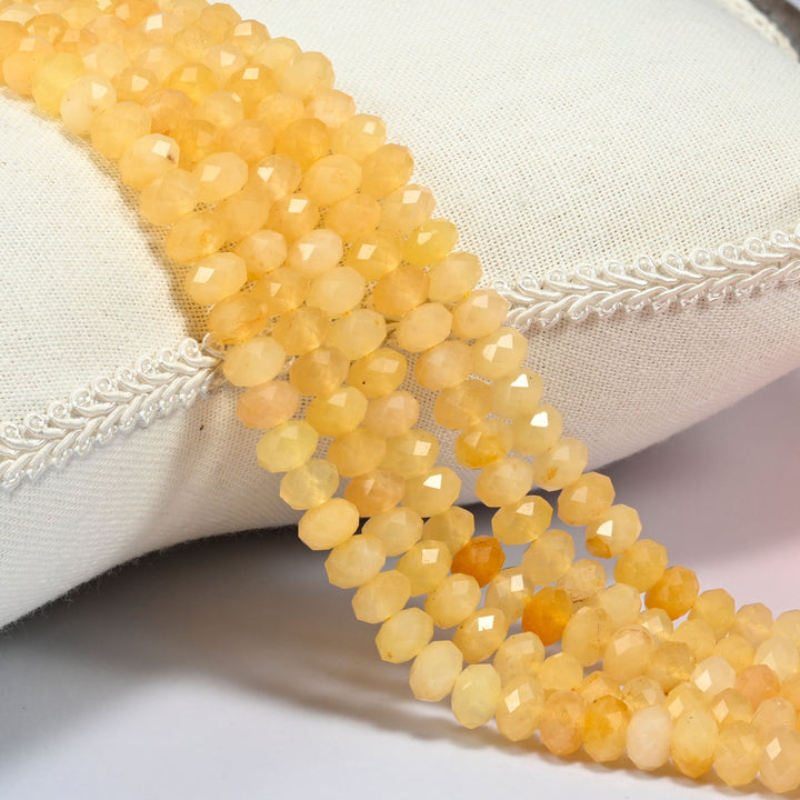 Yellow jade faceted rondelle beads 5x8mm in soft butter yellow, several strands draped over a white cushion