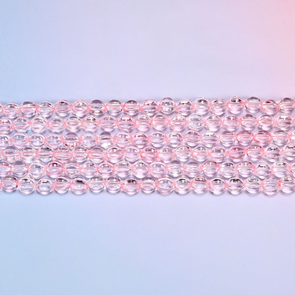 Close-up of 8mm clear pink pumpkin glass beads in four horizontal rows, showing the carved melon ribs.