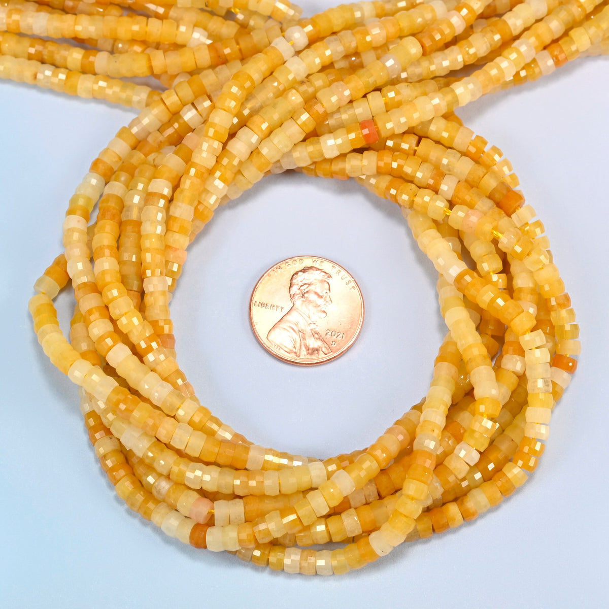 Gold Silk Jade faceted heishi disc beads 2x4mm coiled in a loop around a US penny for scale, close-up of the faceted disc shape