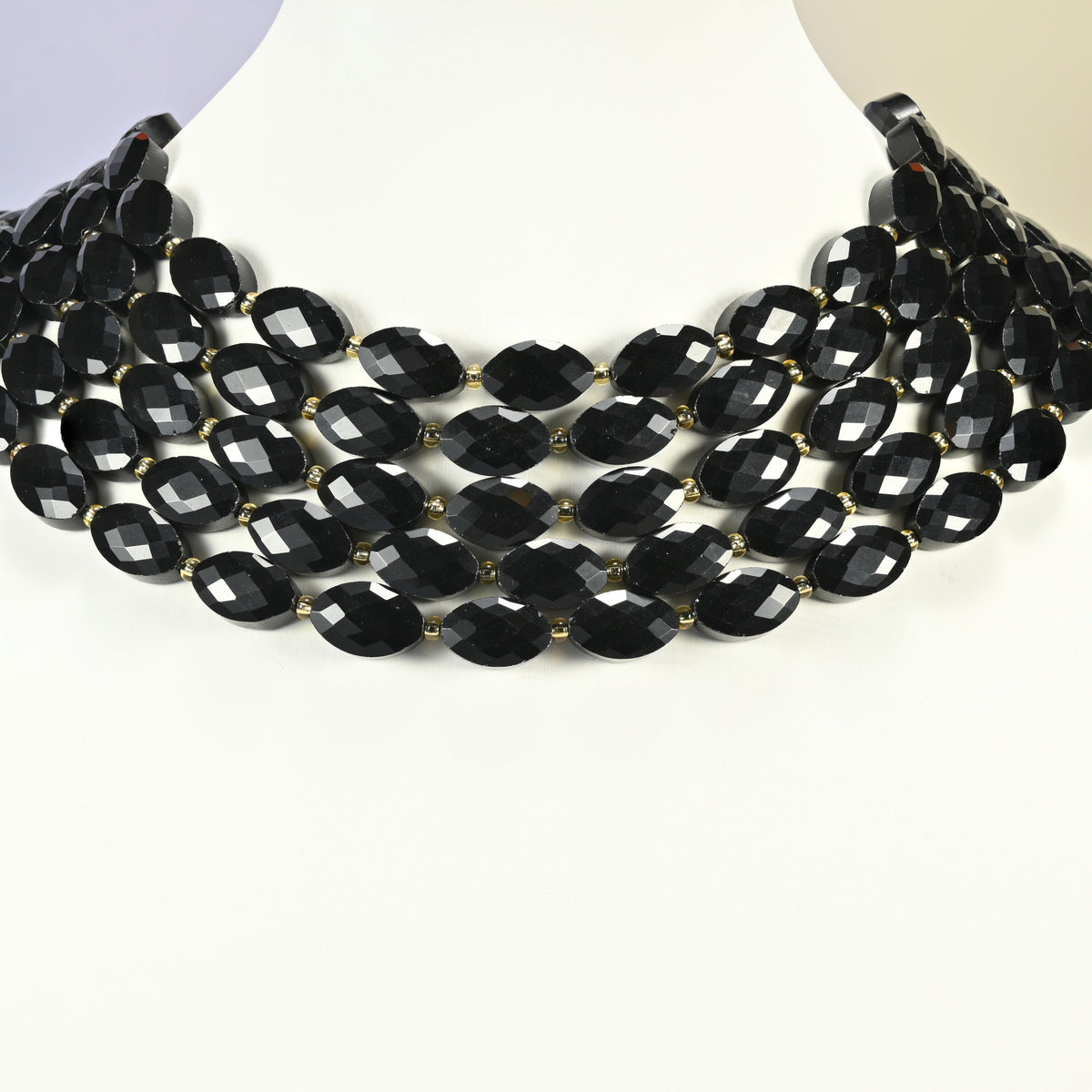 Black onyx faceted flat oval strands arranged as a layered collar on a white display bust, black beads across the neck