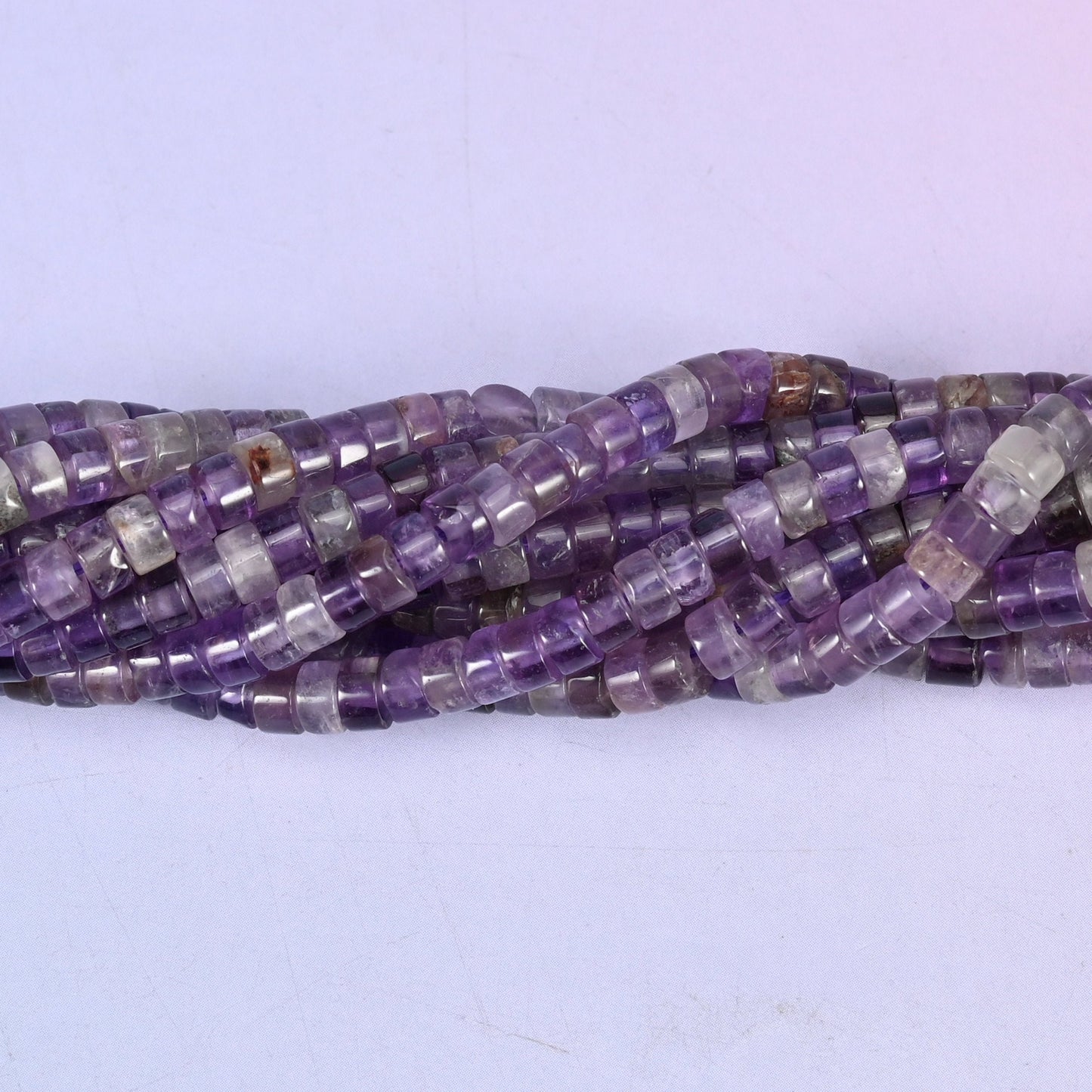 Purple running from pale lilac at one bead to deep violet at the next, translucent enough to glow when light sits behind it, cut into slim polished discs.