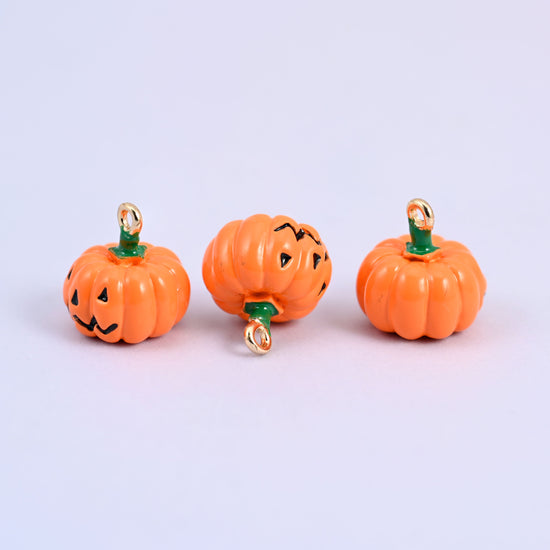 Three enamel pumpkin charms in a row, showing the jack o lantern face and the plain back of the same charm.