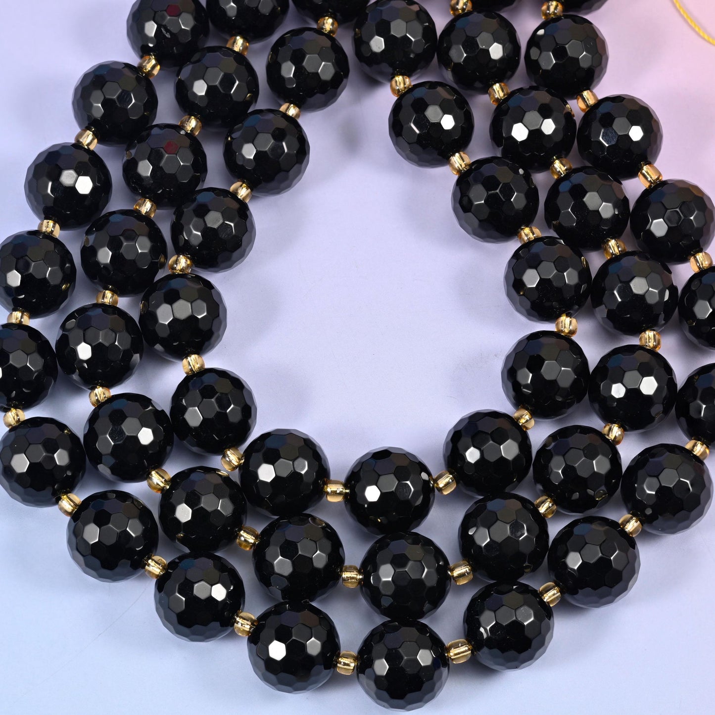 Big jet black rounds covered in dozens of small facets and polished to a mirror gloss, so every plane throws its own hard white highlight, with fine gold-tone spacers set between them on the strand.