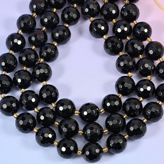 Big jet black rounds covered in dozens of small facets and polished to a mirror gloss, so every plane throws its own hard white highlight, with fine gold-tone spacers set between them on the strand.