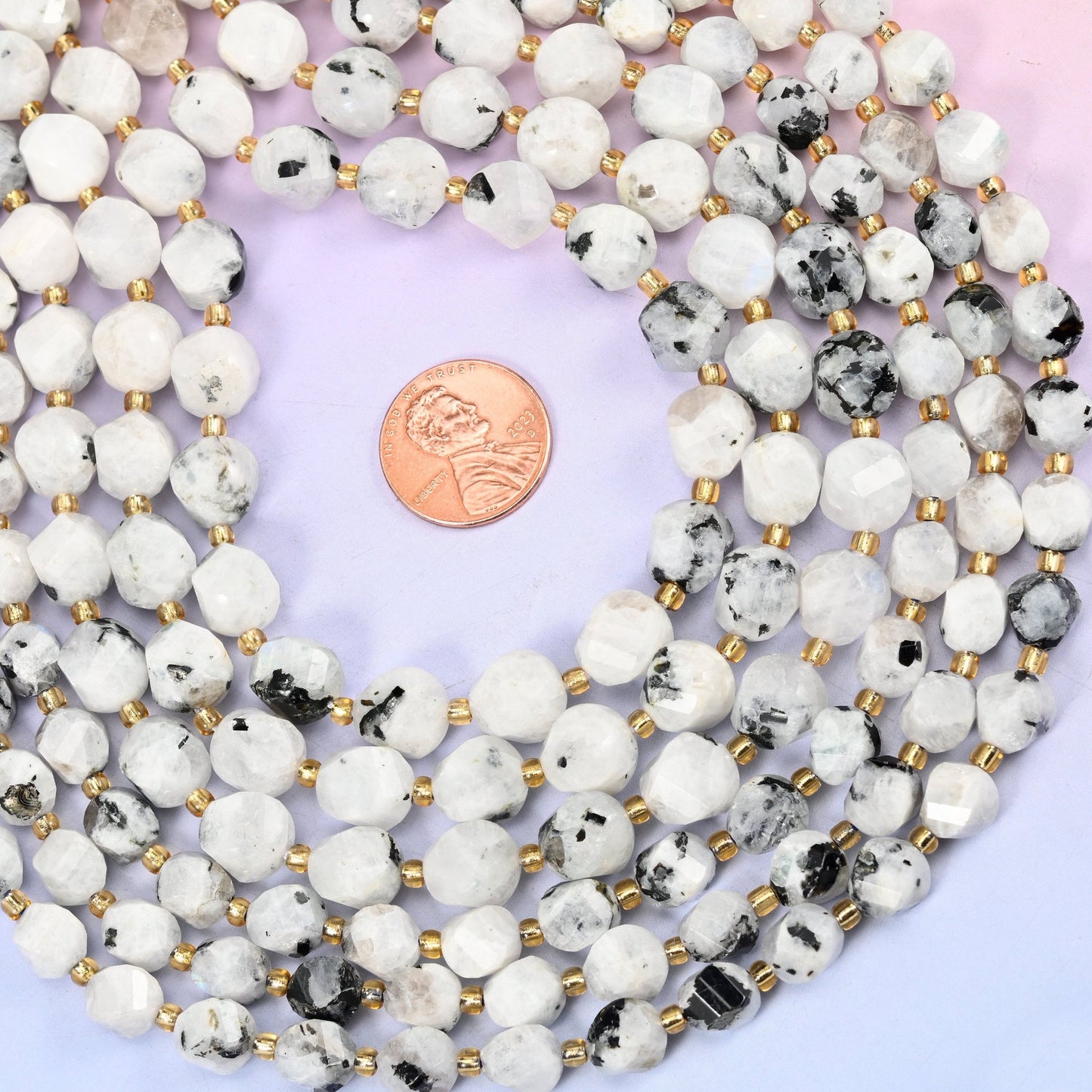 Snow white beads with a soft milky translucency, freckled all over with charcoal and black inclusions, cut into faceted spiral barrels so the light breaks up across the twisting planes