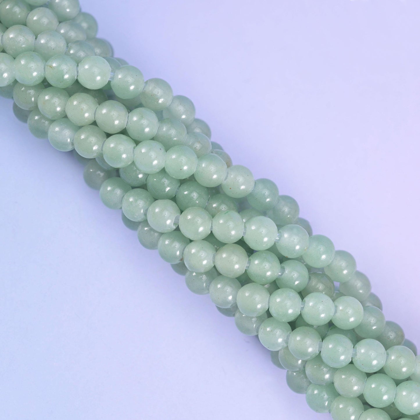 Soft celadon green aventurine rounds, polished to a low glassy sheen and pale enough to read almost seafoam in daylight. Drilled 2.0-2.5mm, so leather, hemp and thick elastic pass straight through.