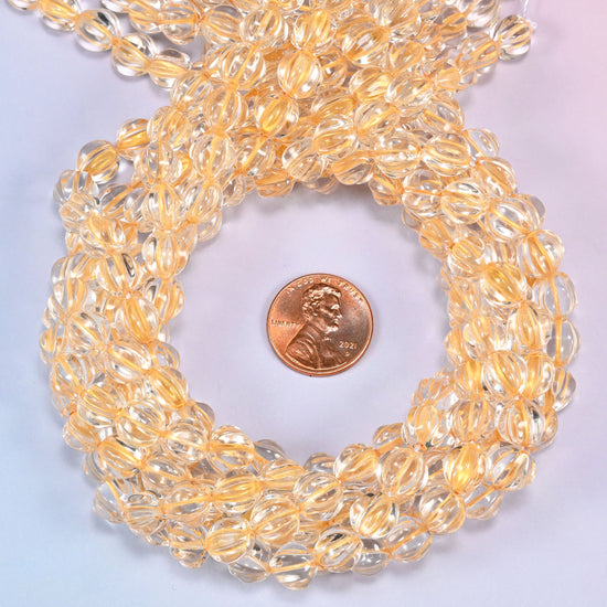 Clear gold pumpkin glass beads coiled tightly, shown with a US penny in the open center for scale.