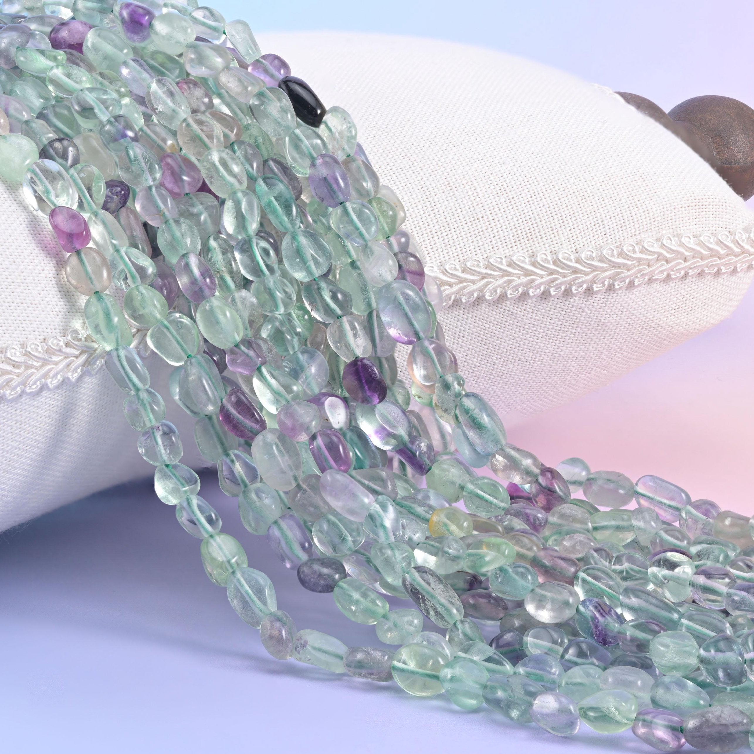 Mint green and purple fluorite nugget strands spilling over a white cushion