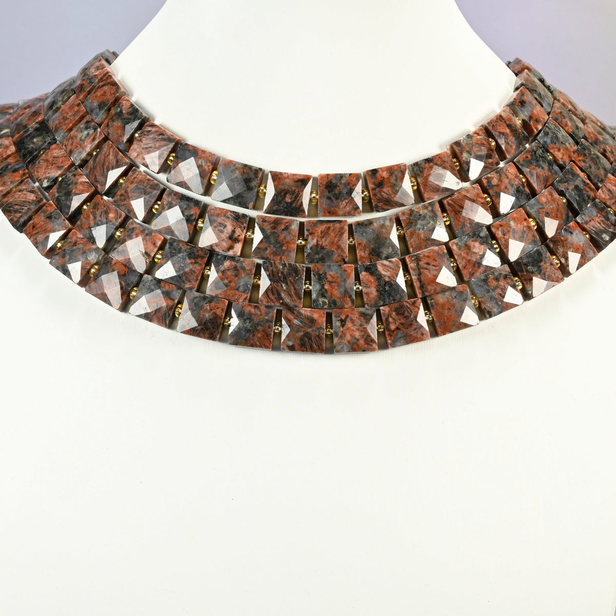 Natural red sesame jasper faceted flat square strands arranged as a layered collar on a white display bust, brick red beads across the neck
