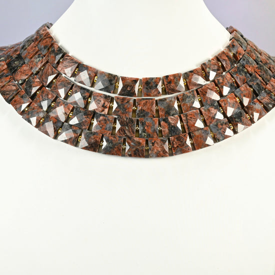 Natural red sesame jasper faceted flat square strands arranged as a layered collar on a white display bust, brick red beads across the neck