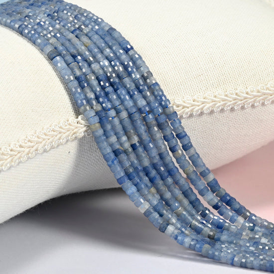 Blue aventurine faceted heishi disc beads 2x4mm, several strands draped over a white cushion