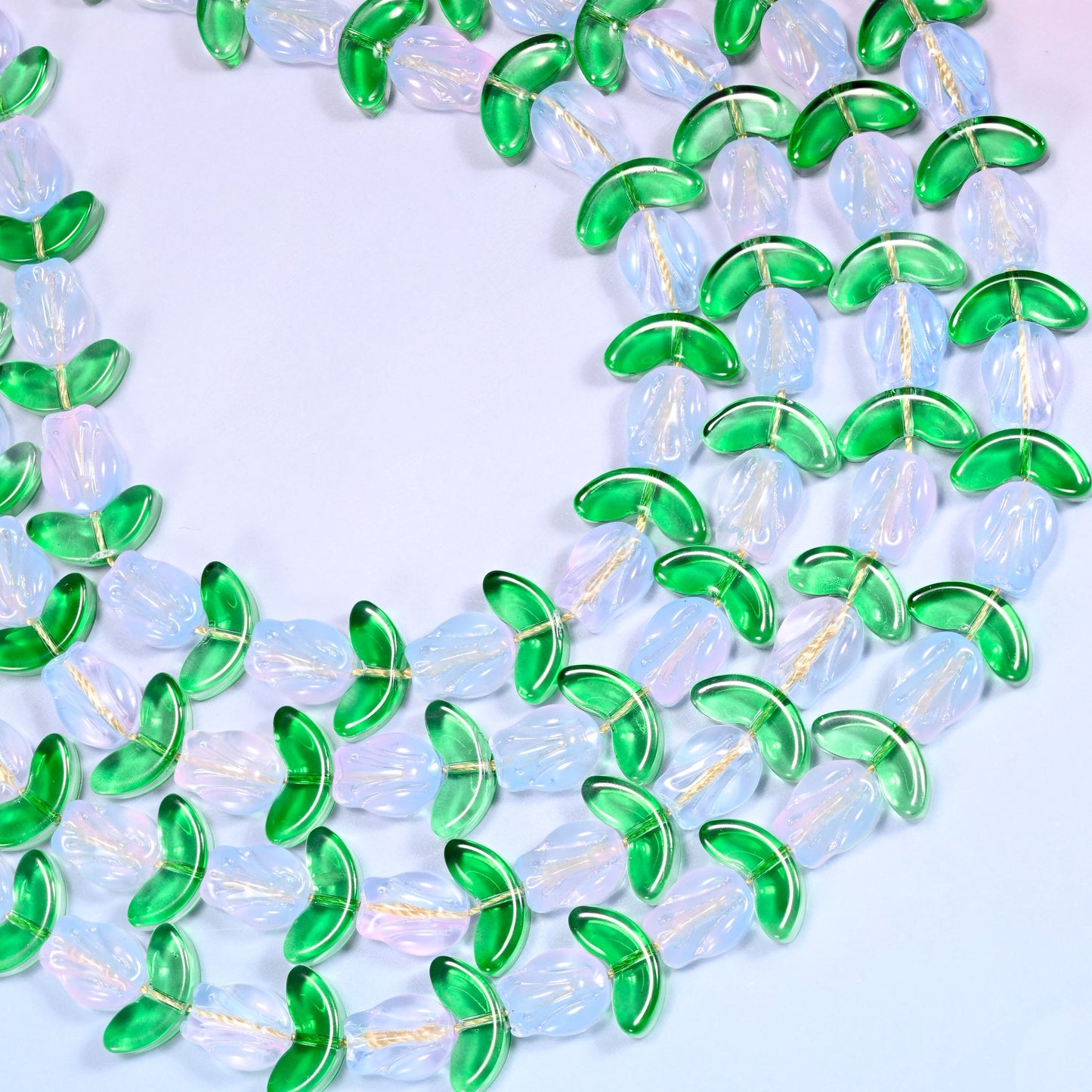 Wide circular coil of white tulip and green leaf glass bead strands forming a full wreath shape on a lavender background.
