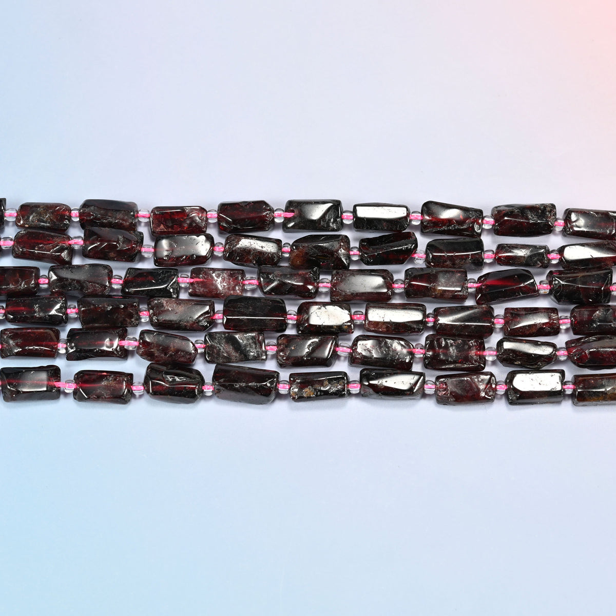 Several strands of red garnet tube beads laid in straight rows with pink seed bead spacers