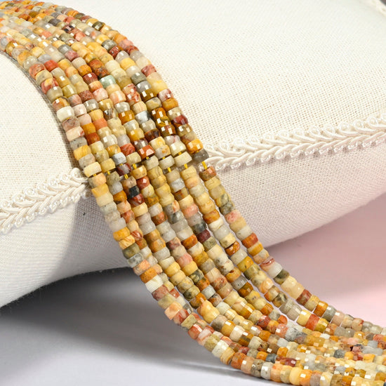 Crazy agate faceted heishi disc beads 2x4mm, several strands draped over a white cushion