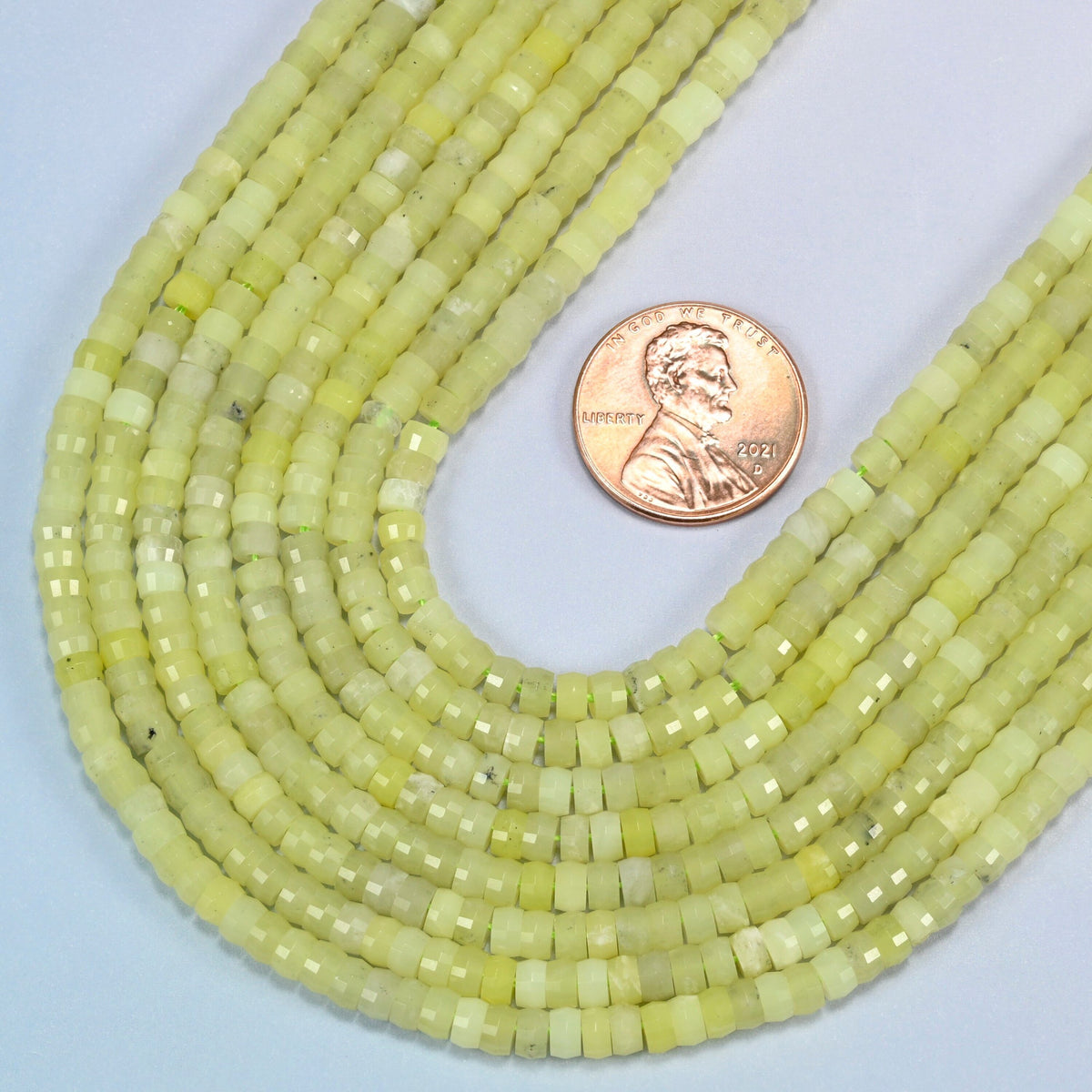 Close view of Lemon Jade faceted heishi disc strands curving beside a US penny for scale