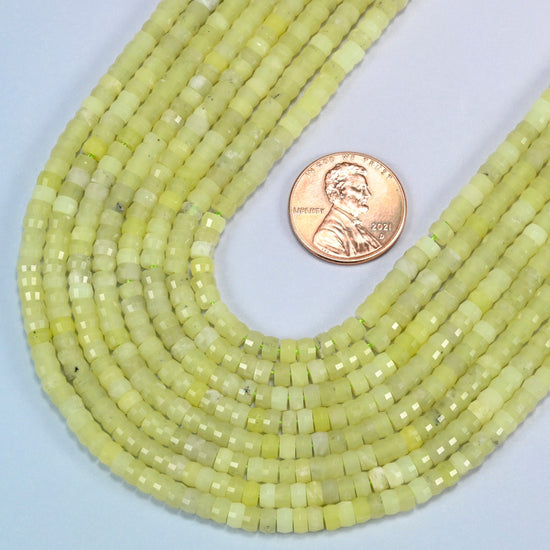 Close view of Lemon Jade faceted heishi disc strands curving beside a US penny for scale