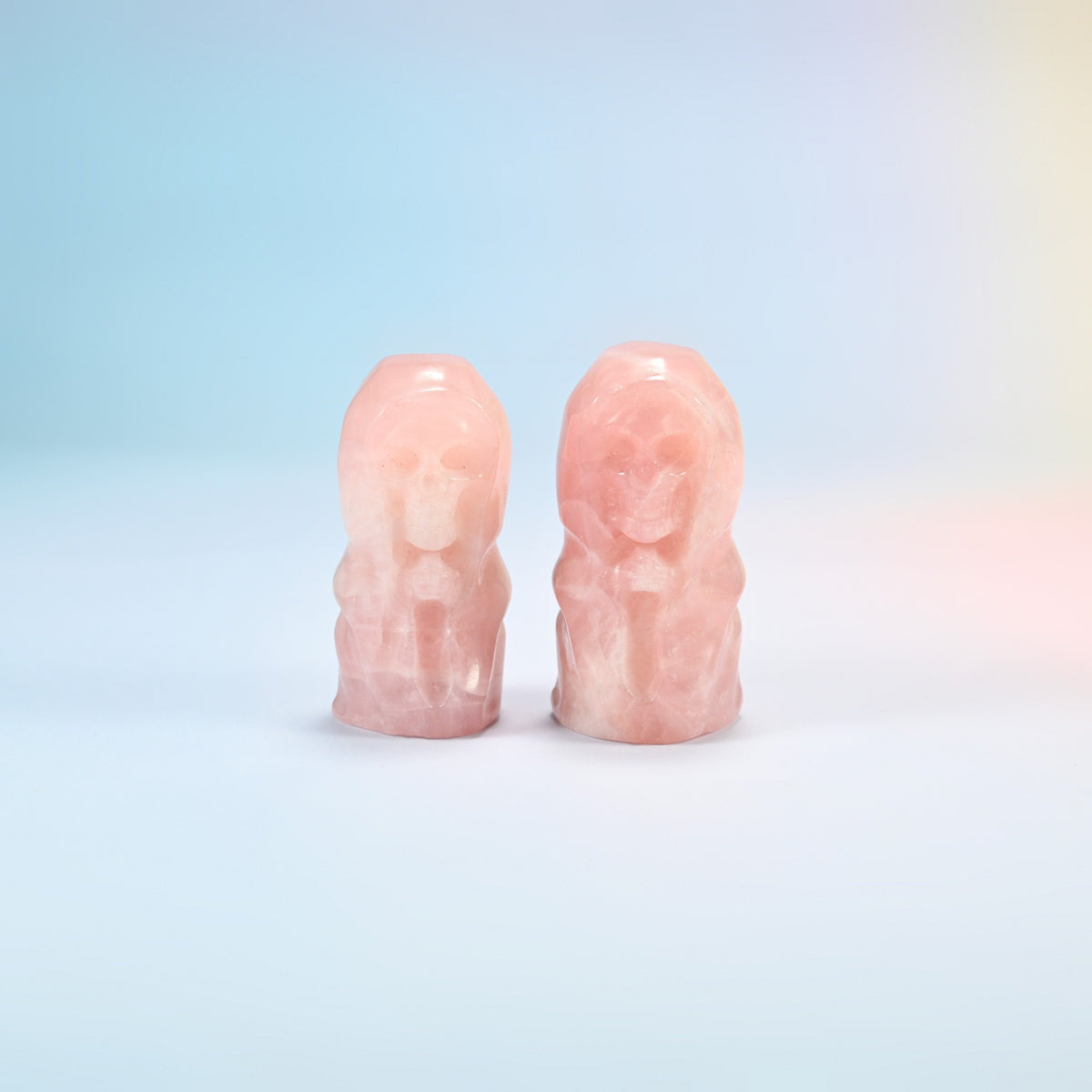 Two natural rose quartz hooded skull carvings in light pink, polished smooth