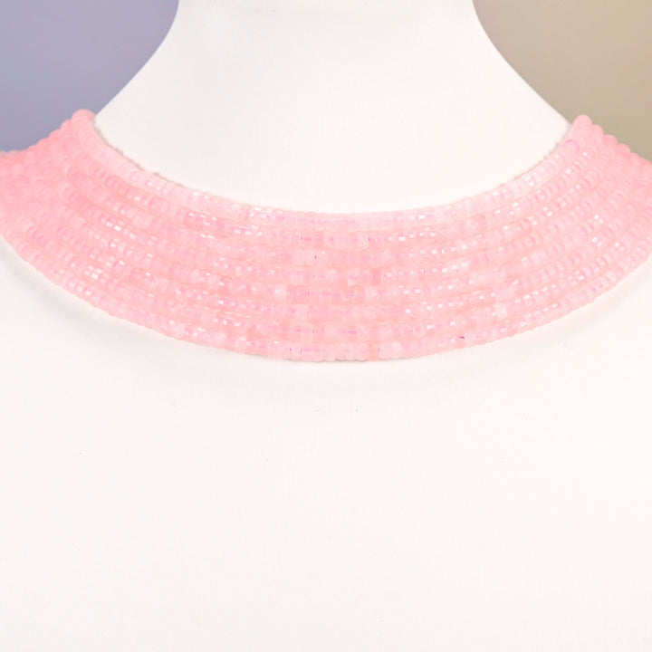 Rose quartz faceted heishi disc strands arranged as a layered collar on a white display bust, pink beads across the neck