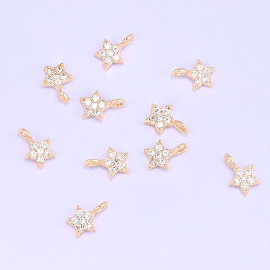 Small gold charms, nine 18K gold plated star charms with clear cubic zirconia scattered on a pale backdrop