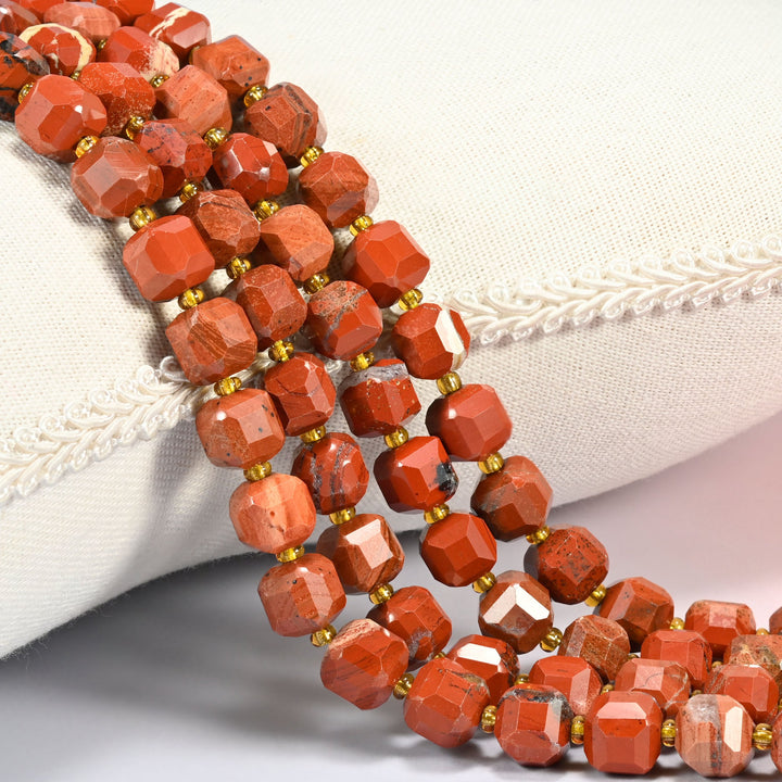 Flower red jasper faceted cube beads 8mm with small gold spacer beads, several strands draped over a white cushion