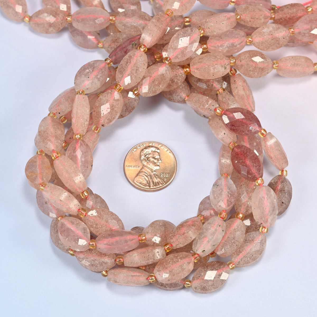 Strawberry quartz faceted flat oval beads 9x14mm coiled in a loop around a US penny for scale, close-up of the faceted flat oval shape