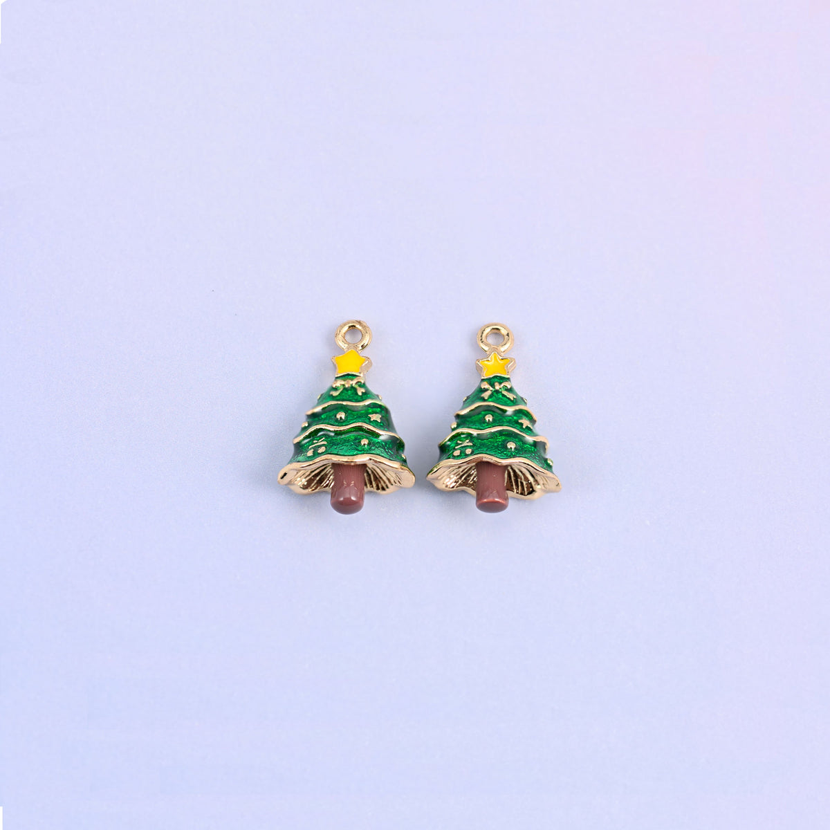Two christmas tree charms side by side, green enamel over 18K gold plated brass with yellow star toppers and brown trunks.