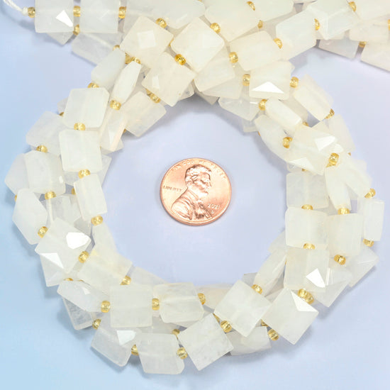 Clear quartz faceted flat square beads 10x10mm coiled in a loop around a US penny for scale, close-up of the faceted flat square shape
